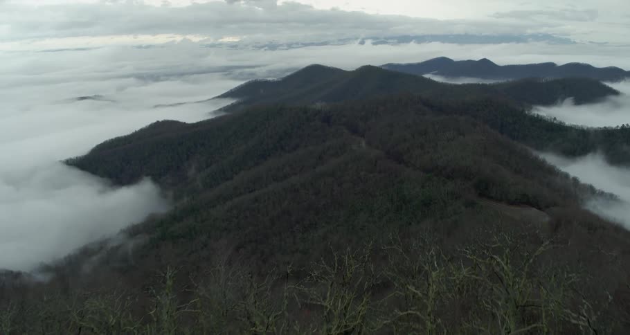 An aerial view of clouds moving across hills and a forest area