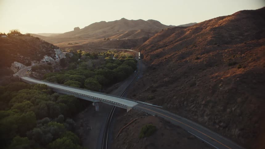 A train travels along the side of mountains and under a highway