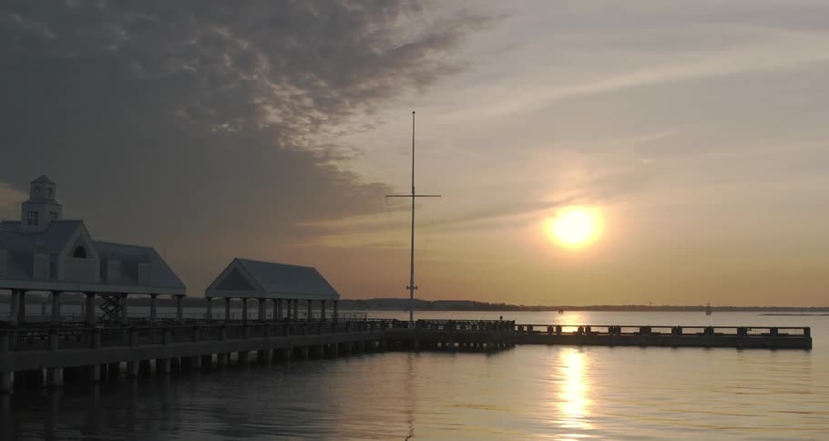 Palm trees along the coast as the sun sets over the water and boardwalk to the pier