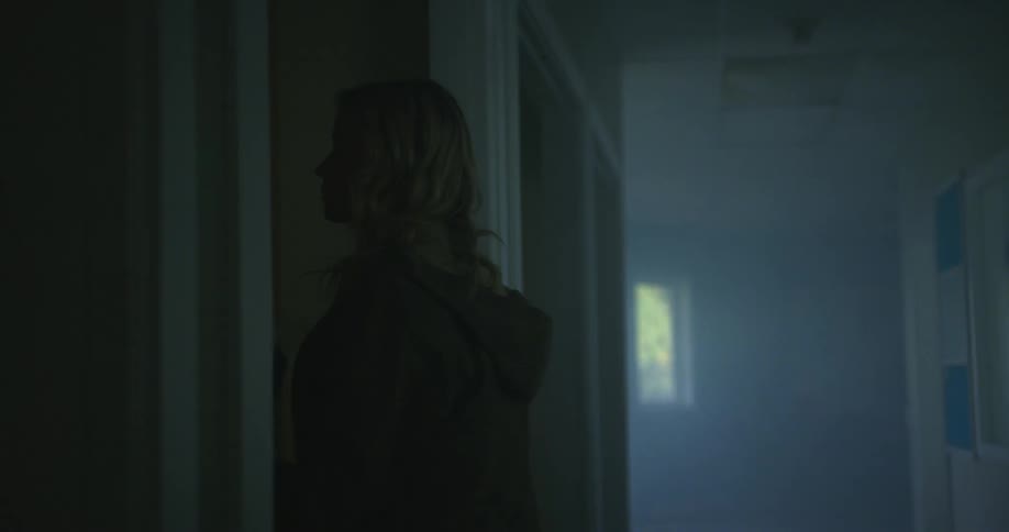A woman walks into a darkened hallway picks up papers and walks back toward the exit