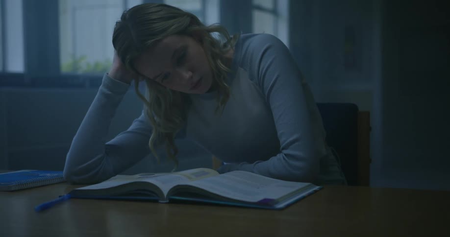 A woman reads a school book while sitting at a work table indoors