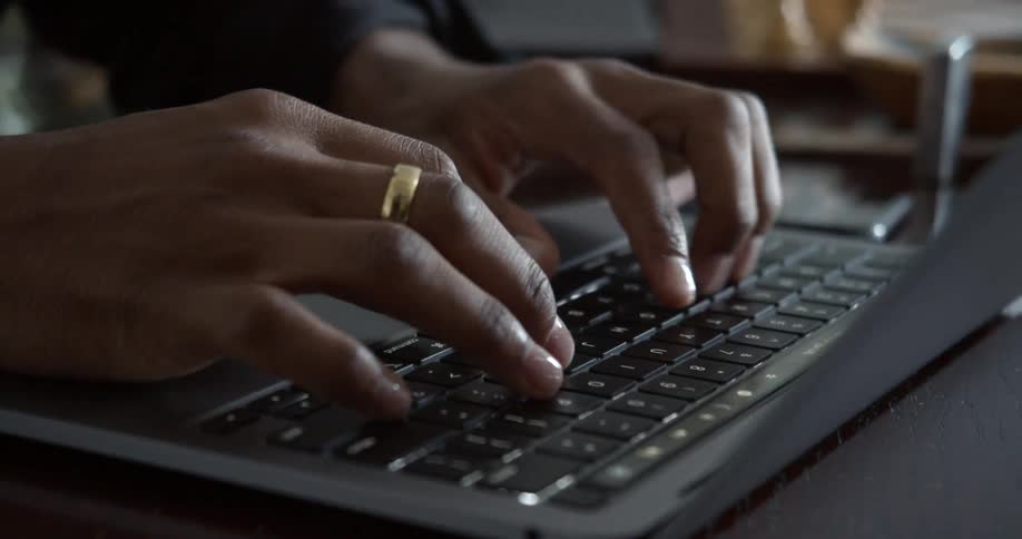 Person wearing ring types on laptop set on dark wooden surface