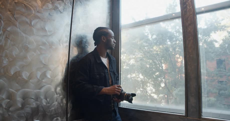 A man holds onto his camera while riding an elevator with glass windows