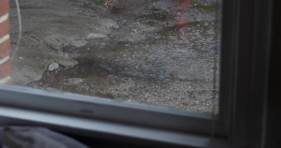 Rain forming puddles is seen through a window