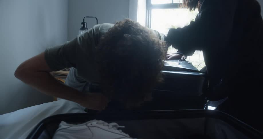 A young man and woman struggle to close a suitcase and then highfive when its shut