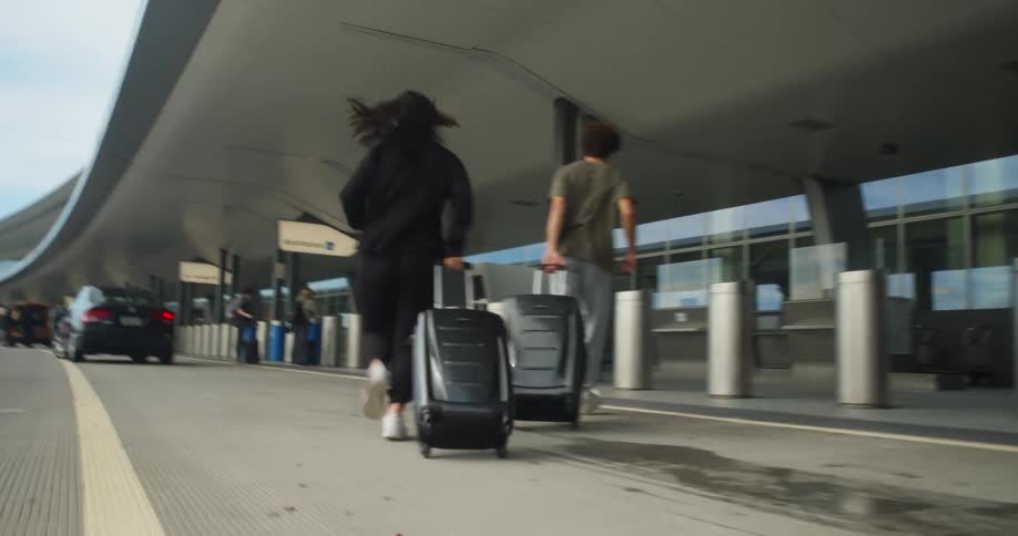 A man and woman pull their luggage behind them as they run in to an airport