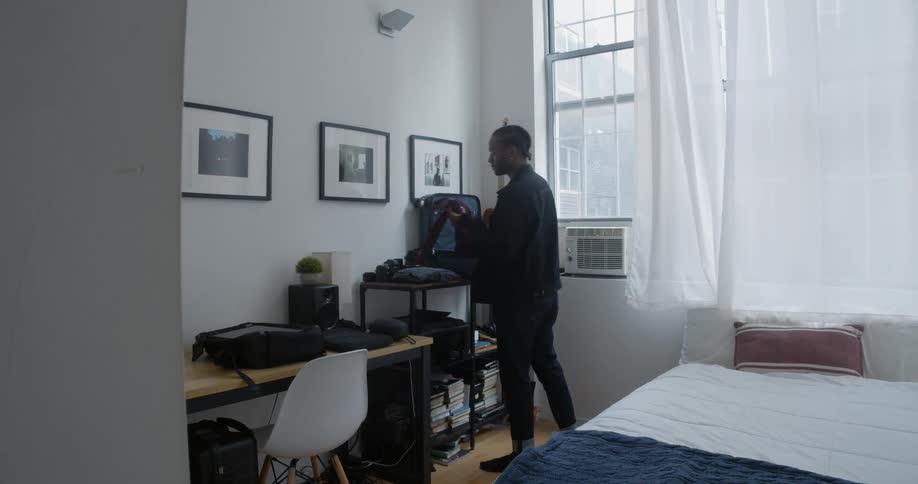 A man is packing a suitcase in his bedroom