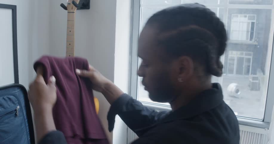A man folds clothes and places them in a suitcase