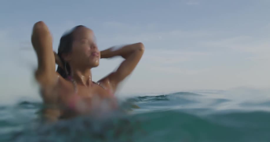 A woman pushes her hair off her face with her hands as she swims up and surfaces