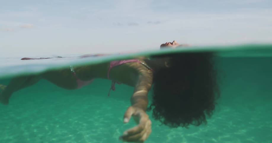 A woman in a bikini floats in the ocean with her arms spread out wide beside her