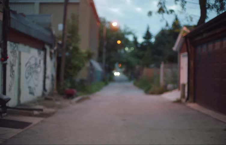 Woman wearing backpack walks along alley passing garages and graffiti covered walls