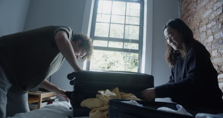 A man and woman try to fit the clothes in the luggage