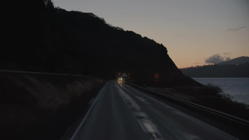 A car drives through a picturesque tunnel before the sun rises next to a large river deep in the pacific Northwest