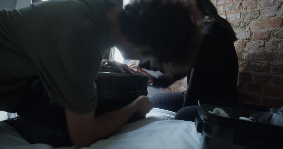 Man and woman smile while trying to close suitcase sitting on bed