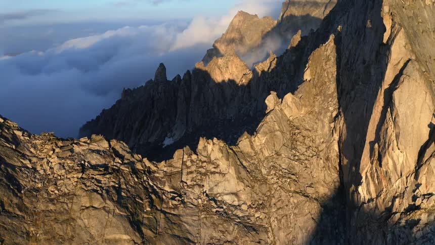 The sun shines on jagged mountain ridges above a layer of cloud cover