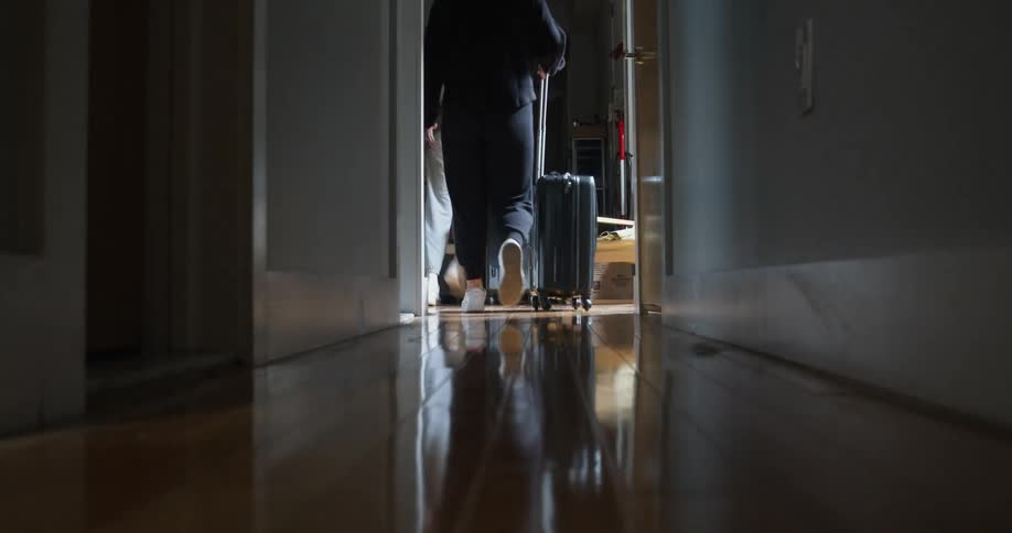 Two people roll suitcase down hallway and leave home