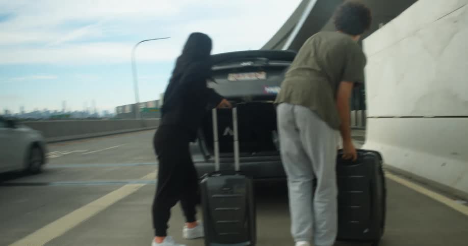 A man and woman get out of the back of a car and go to the trunk and get luggage out and walk towards the airport