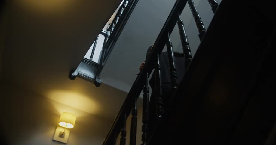 A man and woman each drag and carry luggage down a stairwell in an apartment building