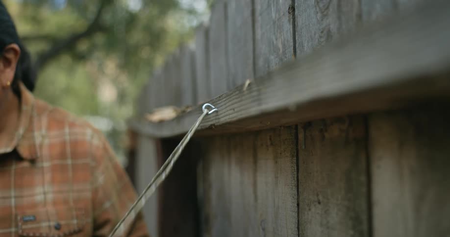 Man runs cord through hook stuck into wooden fence