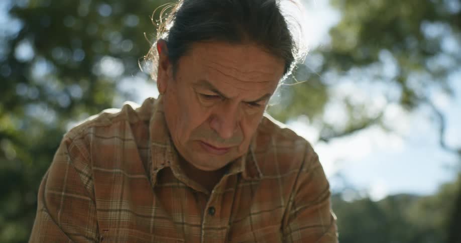 Man with long hair and brown plaid shirt works in garden