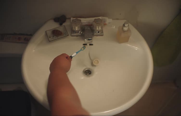 A person rinsing off a toothbrush in a sink