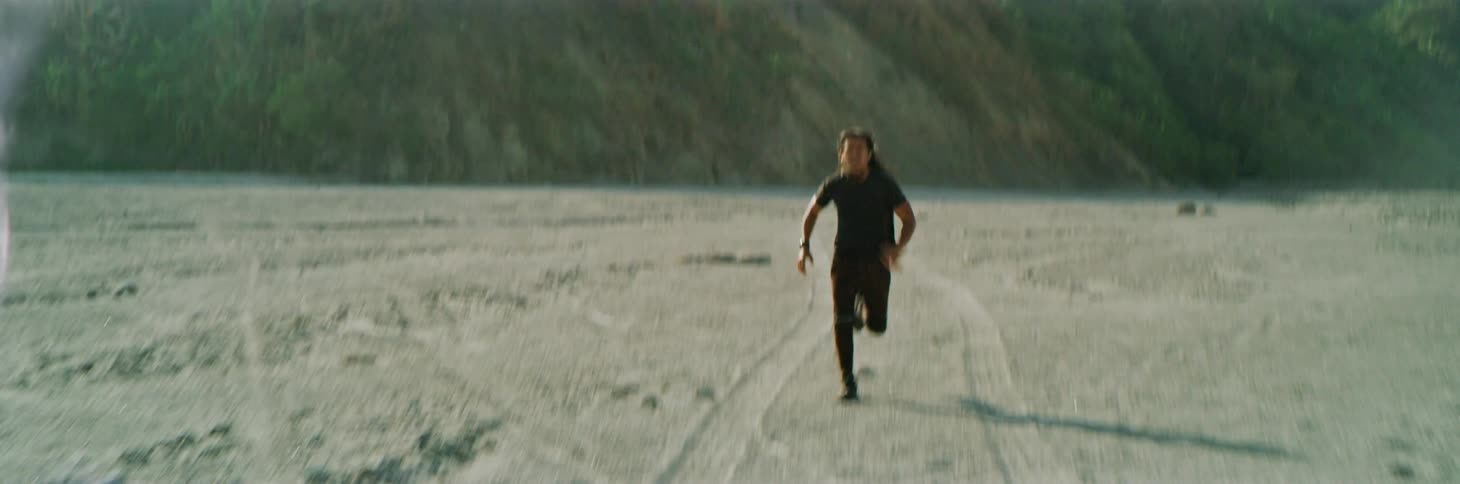 Man runs across sand in between tire tracks with slope in background