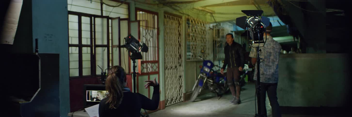 A director sitting by a video display calls the actor over to discuss the script in her hand