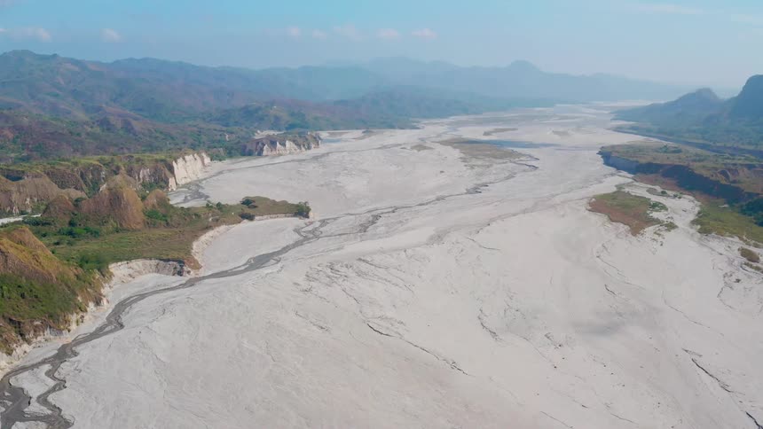 An aerial view of a large dry riverbed in a mountain landscape on a hazy day
