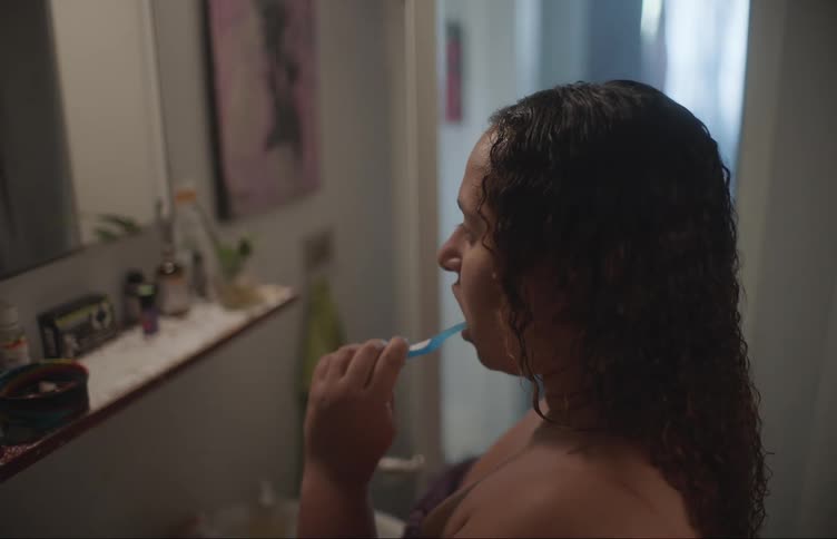 Woman with curly hair brushes her teeth in the bathroom