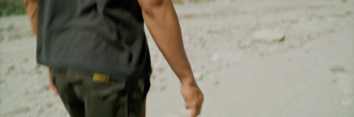 Man walks barefoot across sand toward mountains casting shadow
