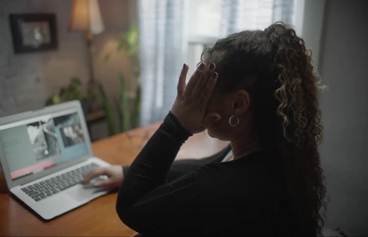 Woman with curly hair and black sweater typing on laptop closes the laptop in room