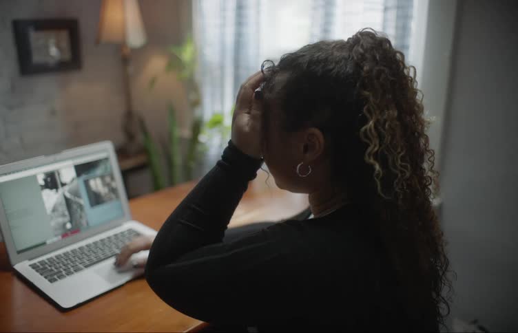 A woman is sitting at a desk using a laptop while at home during the daytime