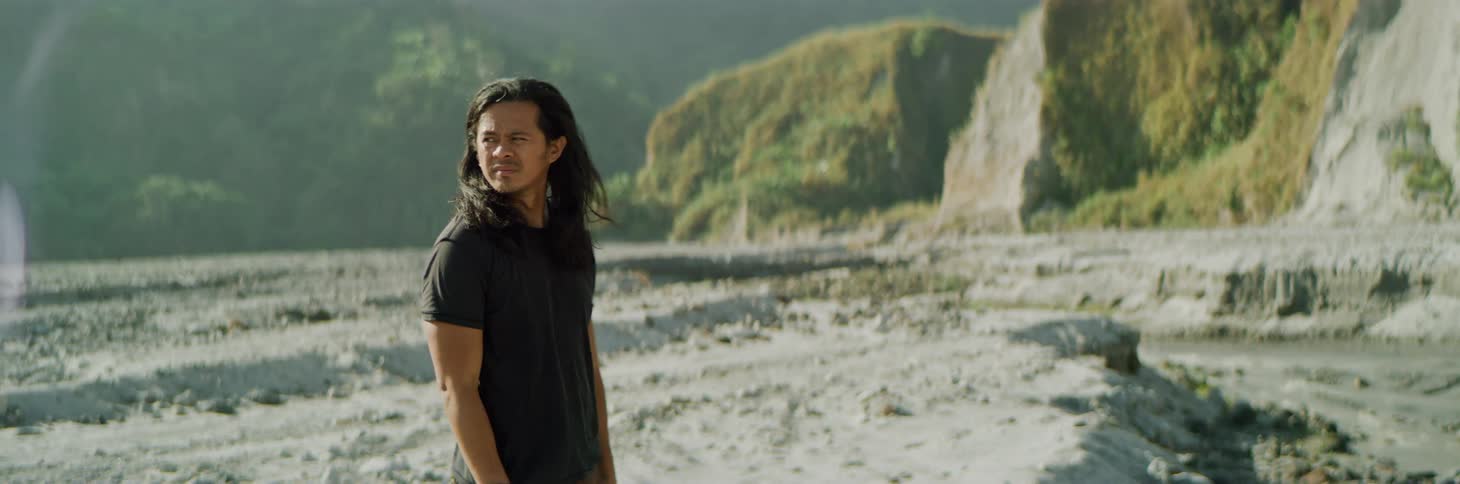 Long haired young man standing on barren plain near the mountains