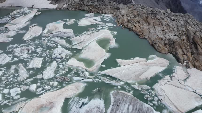 An aerial view of a pool of water and ice on a mountainous rocky terrain in the daytime