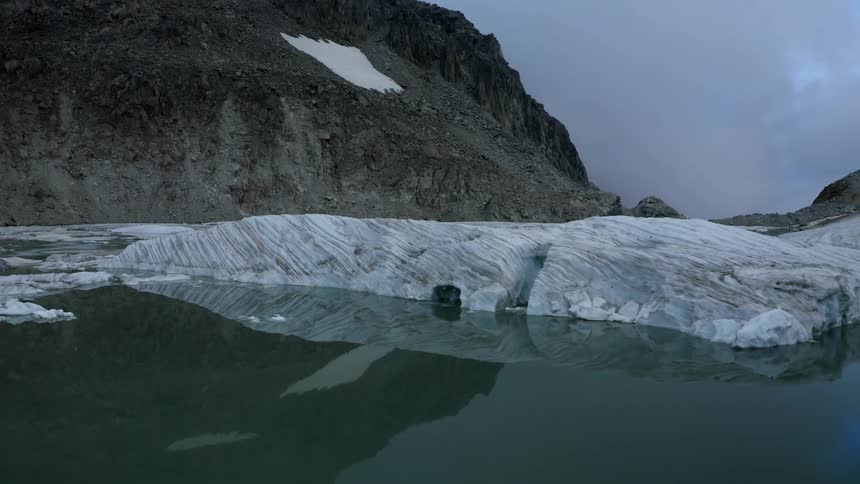Ice floats on reflective calm waters near promontory with glowing green area among overcast sky
