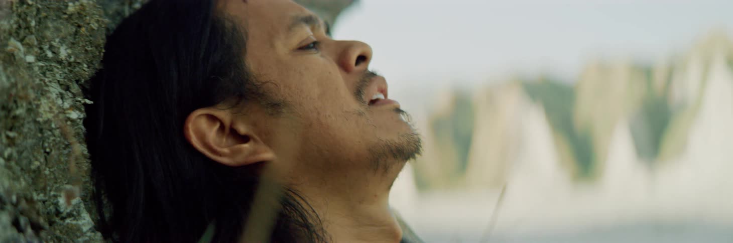 A man with his head back against a rock gasps and looks in despair