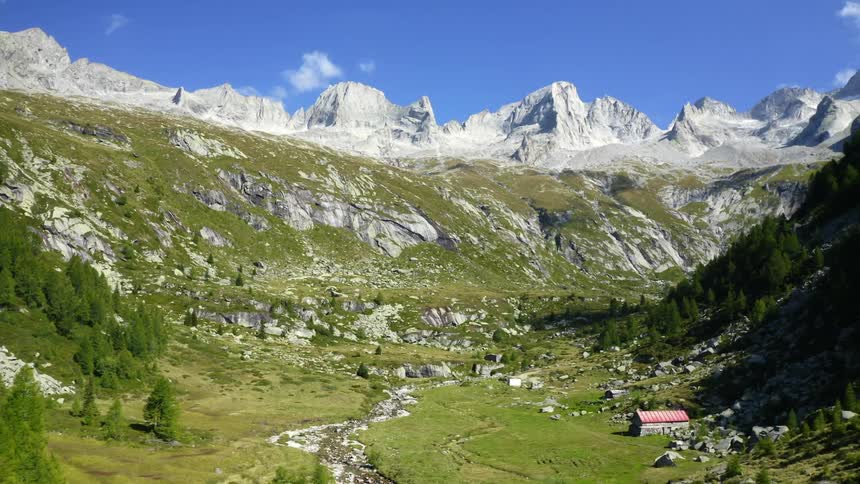 Snow capped mountains tower over valley with river winding past red roofed building