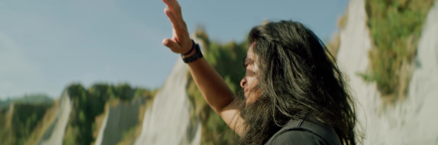 Young man with long hair shields his eyes from the sunlight with his hand near a mountain