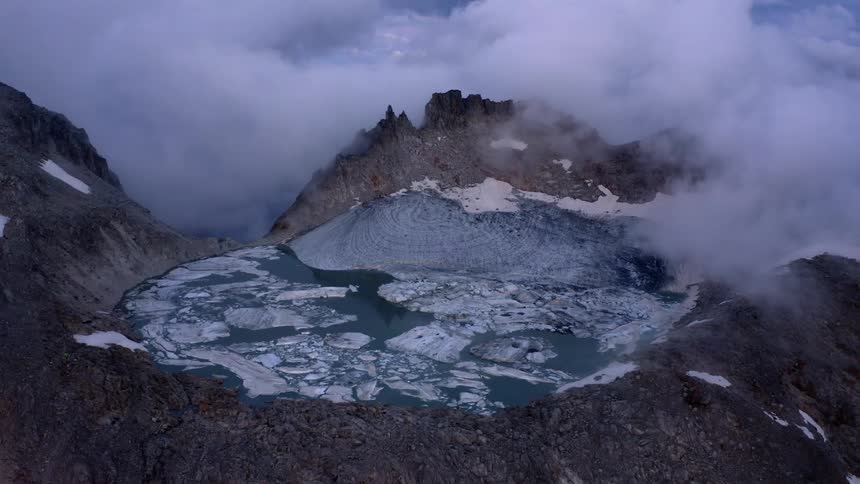 Aerial view of ice sheets floating on a lake atop a mountain covered in clouds