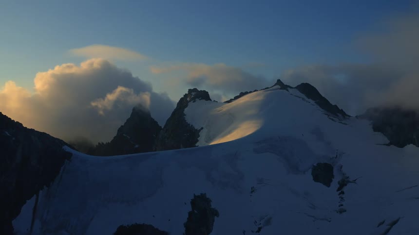 Clouds float around rocky jagged snow covered mountain ridge