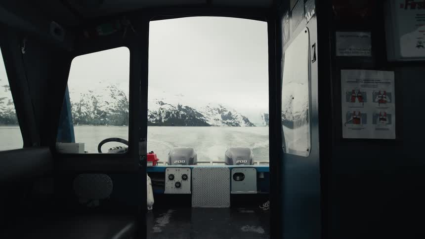 Cabin of a boat driving over a lake near the snow covered peaks of a mountain range