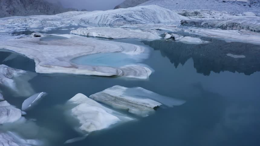 Snow and ice cover a significant portion of the ocean near a mountain