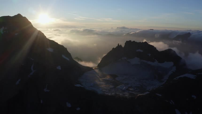 The sun shines through the clouds over mountains peaking high in the sky