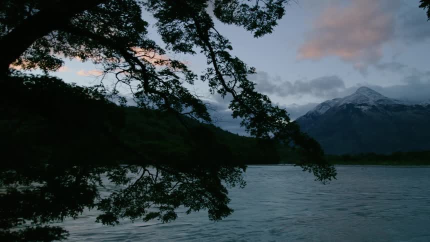 Blue hour panning shot of untouched river waters flowing directly towards snow capped mountains