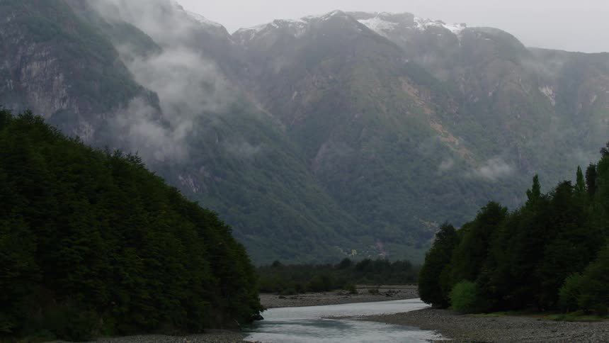 A creek winds through a forest below a mountain range