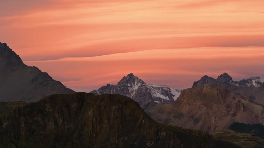 Epic technicolor Time lapse of lenticular clouds waving over the jagged peaks of a snow covered mountain range at sunset