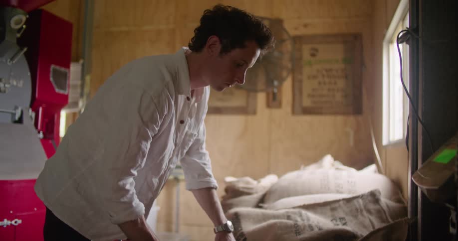 Young man operating machinery for processing coffee beans on a warehouse
