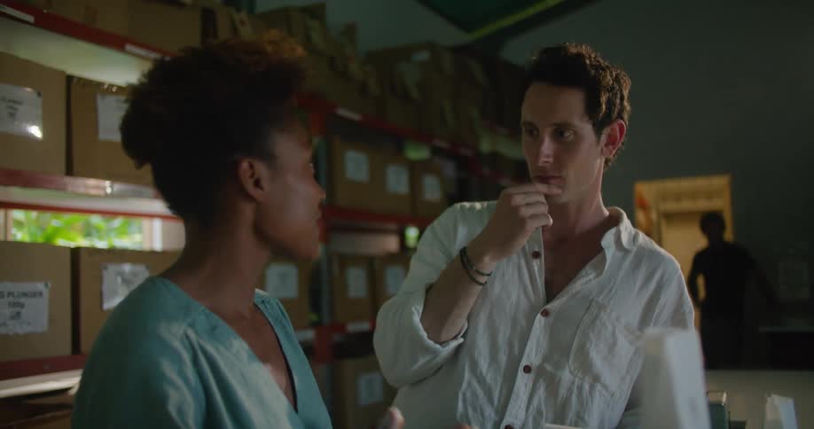 Man with white shirt and woman with curly hair earring and light blue shirttalk to each other in front of shelves with boxes in coffee warehouse