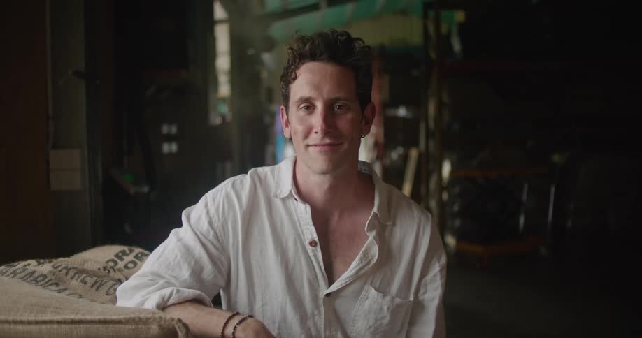 A man smiles as he poses while sitting his armed propped on a table