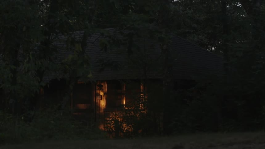 A dark area has a house lit in the distance